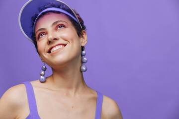Portrait of a sporty fashion woman posing smiling in a purple sports suit for yoga and a transparent cap on a purple background monochrome