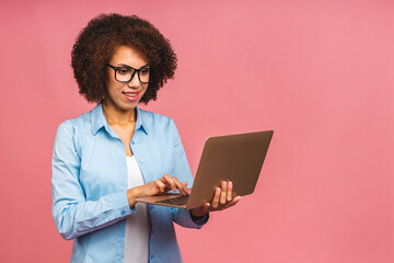 Young african american black positive cool lady with curly hair using laptop and smiling isolated over pink background.