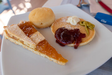 Delicious pancake with strawberry jam bun and apricot tart on white plate
