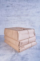 A stack of large classic-looking parcels wrapped in kraft paper and tied with natural jute twine against a wooden wall with white shabby paint. Packing, gifts, delivery