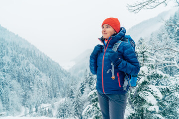 Female backpacker with backpack dressed warm down jacket enjoying snowy mountains landscape while...