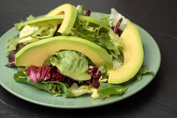 Avocado on the background of salad mix. Fresh salad with arugula, purple lettuce, spinach, frisee, chard leaves and avocado