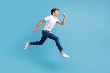 Fototapeta na wymiar Side view of joyous man in sneakers denim outfit running in air hurrying discounts indoor studio shot isolated blue background