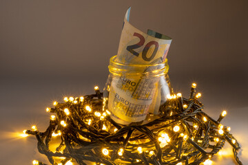 Glass jar with twenty euro banknote on a gray background, on top of led lights. Euro christmas money savings concept.
