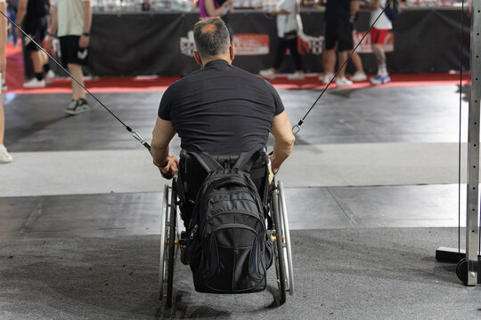 Man Sitting in a Wheelchair with a Backpack attached doing Arm and Shoulder exercises with Gym Equipment