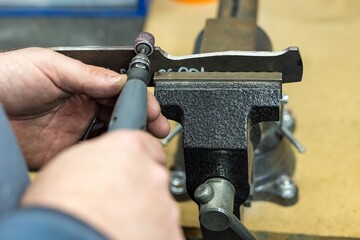 Industrial tool worker grinds a wood handle on a rotating belt sander, he makes a knife handle.