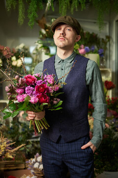 Attractive cheerful caucasian male in peaked cap and vintage clothes from 20s holding beautiful bouquet of red and violet flowers. Mother's Day or Valentine's Day concept. High quality image