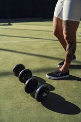Vertical closeup of man's tattooed feet next to dumbbells on green grass in an outdoor gym