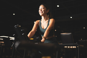 Fototapeta na wymiar Young Asian woman on a bicycle doing spinning in a gym. Young woman exercising on stationary bike.