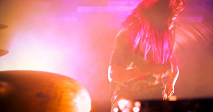 Young beautiful girl vigorously playing drums on the stage. Multicolored strobe lights flicker to the beat of the drums. Camera zooms in on the drummer to the beat of the drum beats
