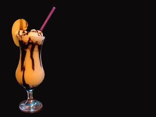 Glass with green apple drink, condensed milk and chocolate sauce with a straw on a black background and copy space