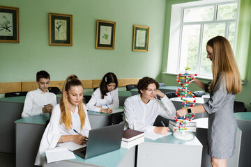 Biology teacher gives a lesson to pupils in classroom. Schoolchildren at biology lesson at school with DNA model on the table. Education at school of biology and chemistry.