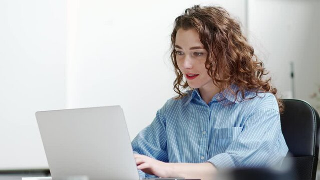 Young happy business woman company employee sitting at desk working on laptop. Smiling female professional worker marketer using computer in corporate modern office managing online data technology.