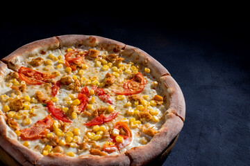 Pizza for children on a cream base with chicken fillet, tomatoes, corn and mozzarella cheese on black background