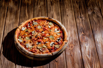 Appetizing pizza with hunting sausages, mozzarella cheese, pickled cucumbers, chili peppers on a tomato base on wood background