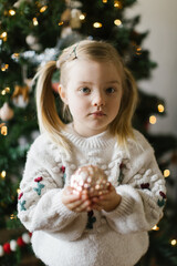 Little girl holding gold ornament in front of christmas tree