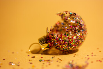 Broken Christmas tree toy, multicolored glitter ball, shards of glass on brown yellow background....