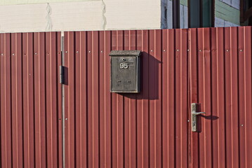 one black mailbox hanging on a red metal fence in the street