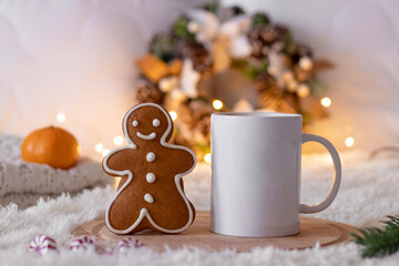 Christmas cozy composition. Gingerbread man cookie, white cup of tea or coffee, Christmas wreath with lights on a white blanket. Selective focus