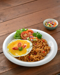 Indomie goreng Indonesian Popular Instant fried Noodle. Served with Sunny Side Egg, Tomato, Cucumber, letucce, and chilli.