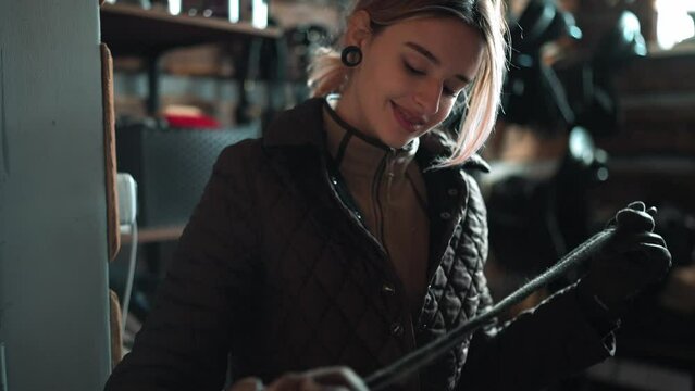 Handsome woman rider wearing gloves twists a riding whip in the stable