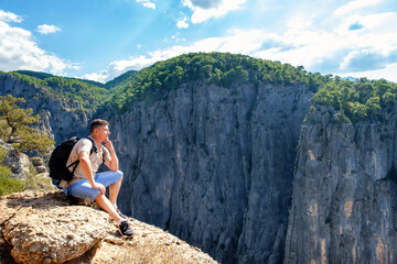 Naklejka premium Side view of tranquil male hiker with backpack sitting on edge of rocky cliff in highlands on summer day