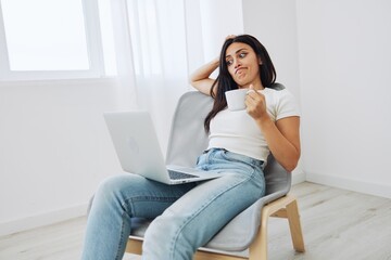 Woman relaxing at home sitting on a chair and watching a movie on her laptop with a cup of tea, autumn mood