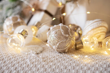 Light bronze glitter Christmas ball on a beige knitted plaid with a garland and Christmas decorations.