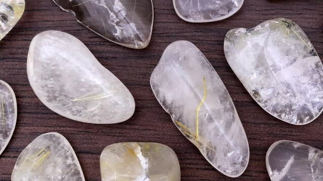 Rutilated quartz rare jewel stones texture on brown varnished wood background. Moving right seamless loop backdrop.