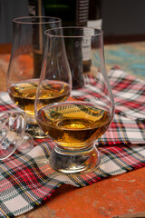 Tulip-shaped tasting glass with dram of Scotch single malt or blended whisky on wooden table with tartan
