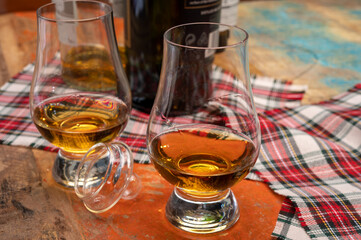 Tulip-shaped tasting glass with dram of Scotch single malt or blended whisky on wooden table with...