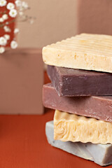 closed shot of a pile of bars of handmade soaps of different colors, with small white flowers on a brown background.