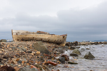A wrecked boat on the shore next to wharf. The boat is in very poor shape and is falling apart. Low tide.