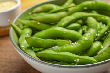 Bowl with green edamame beans in pods on wooden table, closeup