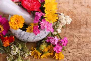 Marble mortar, pestle and different flowers on wooden table, closeup
