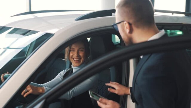 A handsome male consultant with a tablet is talking to a young pretty female client in a car