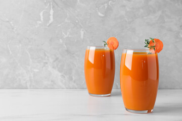 Glasses with healthy carrot juice on white table. Space for text