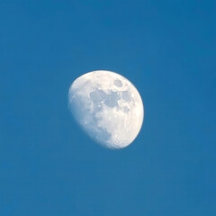 The moon rises in the daytime on the blue sky.