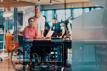 Businesswoman in a wheelchair working in a creative office. Business team in modern coworking office space. Colleagues working in the background at late night.