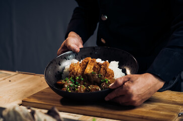 Japanese chicken katsu curry rice, deep fried breast chicken fillet with beef, carrot and potato curry in black plate on wooden table Crispy fried pork cutlet with curry rice  - Japanese food style