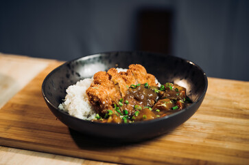 Japanese chicken katsu curry rice, deep fried breast chicken fillet with beef, carrot and potato curry in black plate on wooden table Crispy fried pork cutlet with curry rice  - Japanese food style