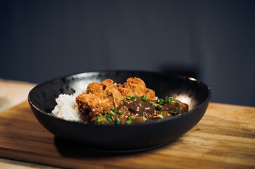 Japanese chicken katsu curry rice, deep fried breast chicken fillet with beef, carrot and potato curry in black plate on wooden table Crispy fried pork cutlet with curry rice  - Japanese food style
