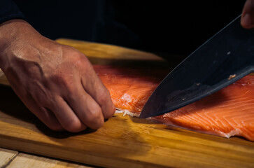 Close up of Chef cook hands chopping salmon fish for traditional Asian cuisine with Japanese knife. Professional Sushi chef cutting seafood japanese chefs are making salmon fish sashimi. dark tone