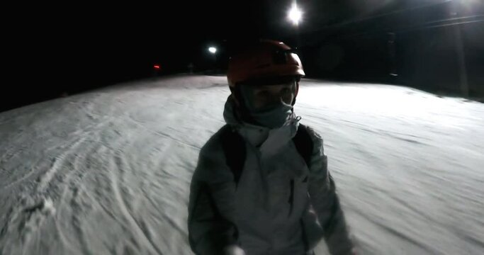 Female skier speeding down the ski slope at night, skiing at night in the lighted ski resort. Mountains views on blurred background
