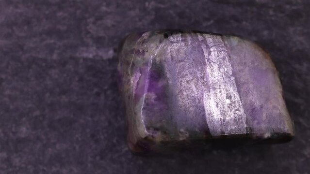 Sugilite jewel stone texture on black stone background. Macro closeup. Moving right seamless loop backdrop.