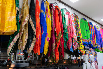 Rajasthani womens clothes are hanging for sale , being displayed in a shop at famous Sardar Market and Ghanta ghar Clock tower in the evening.