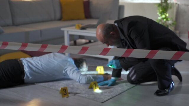 Prosecutor man examining body at crime scene surrounded by barricade tape.
Male prosecutor examining body of victim killed at home and looking at evidence.
