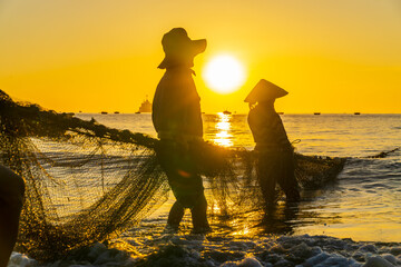 Silhouette of Asian fishermen hailing in nets at sunrise in D Nang, Vietnam
