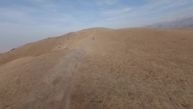 FPV sports drone follow shot SUV car drive rally offroad riding desert mountain adventure sand splash. Aerial chase view cinematic hilly valley dirt road transportation extreme tourism exploration 4k