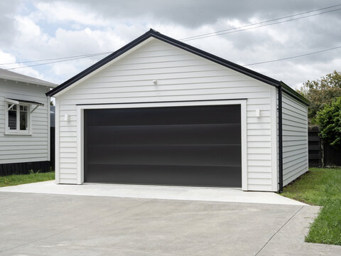 Typical double detached white garage with black tilt-up retractable raised panel metal door and gable metal roof